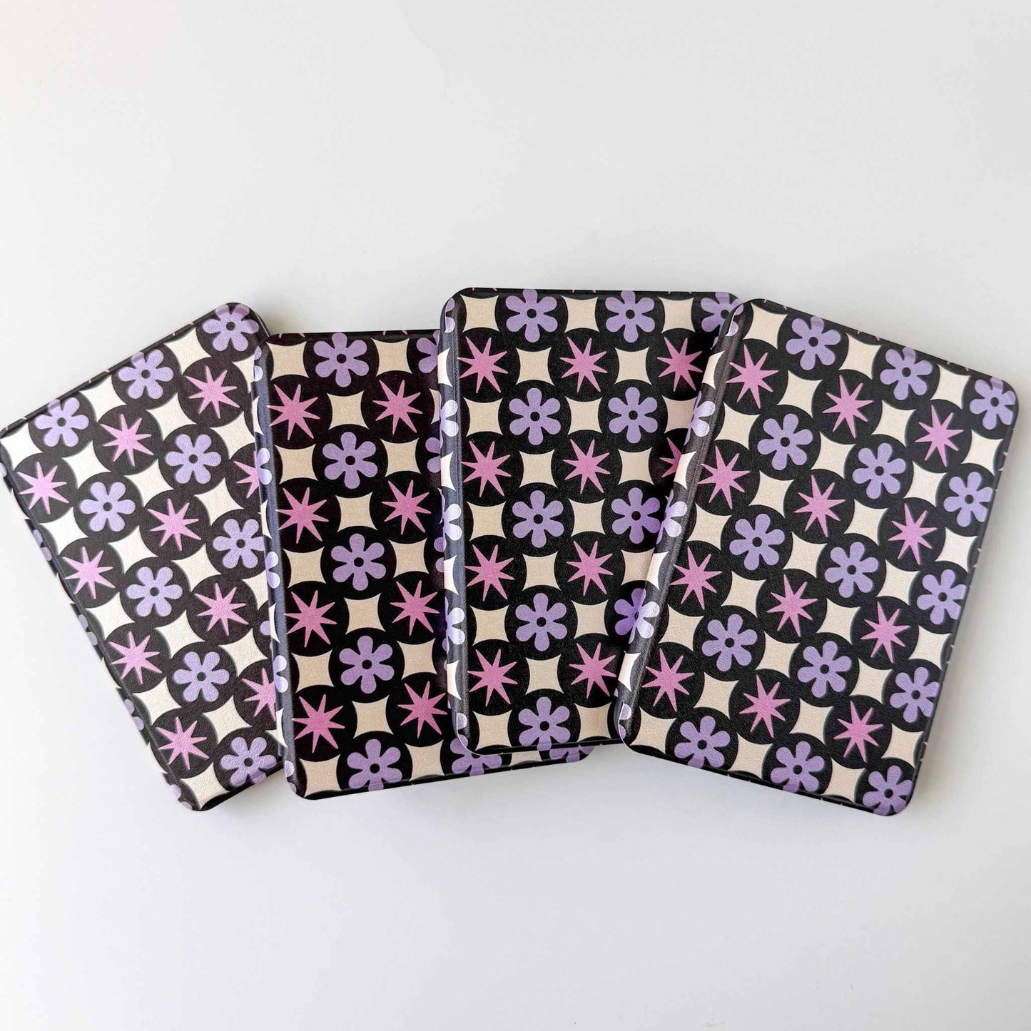 Four patterned kindle cases with purple floral and  black and white geometric designs on a white background