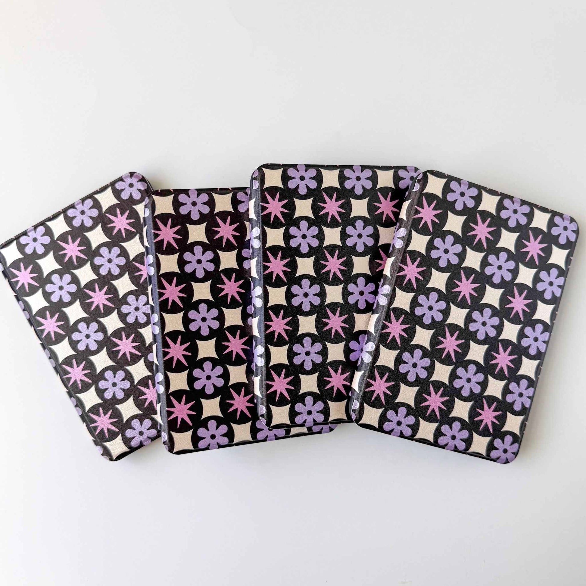 Four patterned kindle cases with purple floral and  black and white geometric designs on a white background