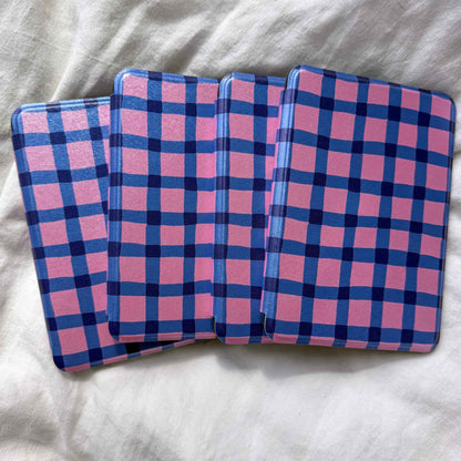 Four pink and blue checkered kindle cases on a white linen surface