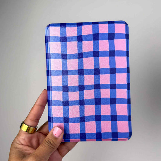 Hand holding a pink and blue checkered kindle case against a gray background
