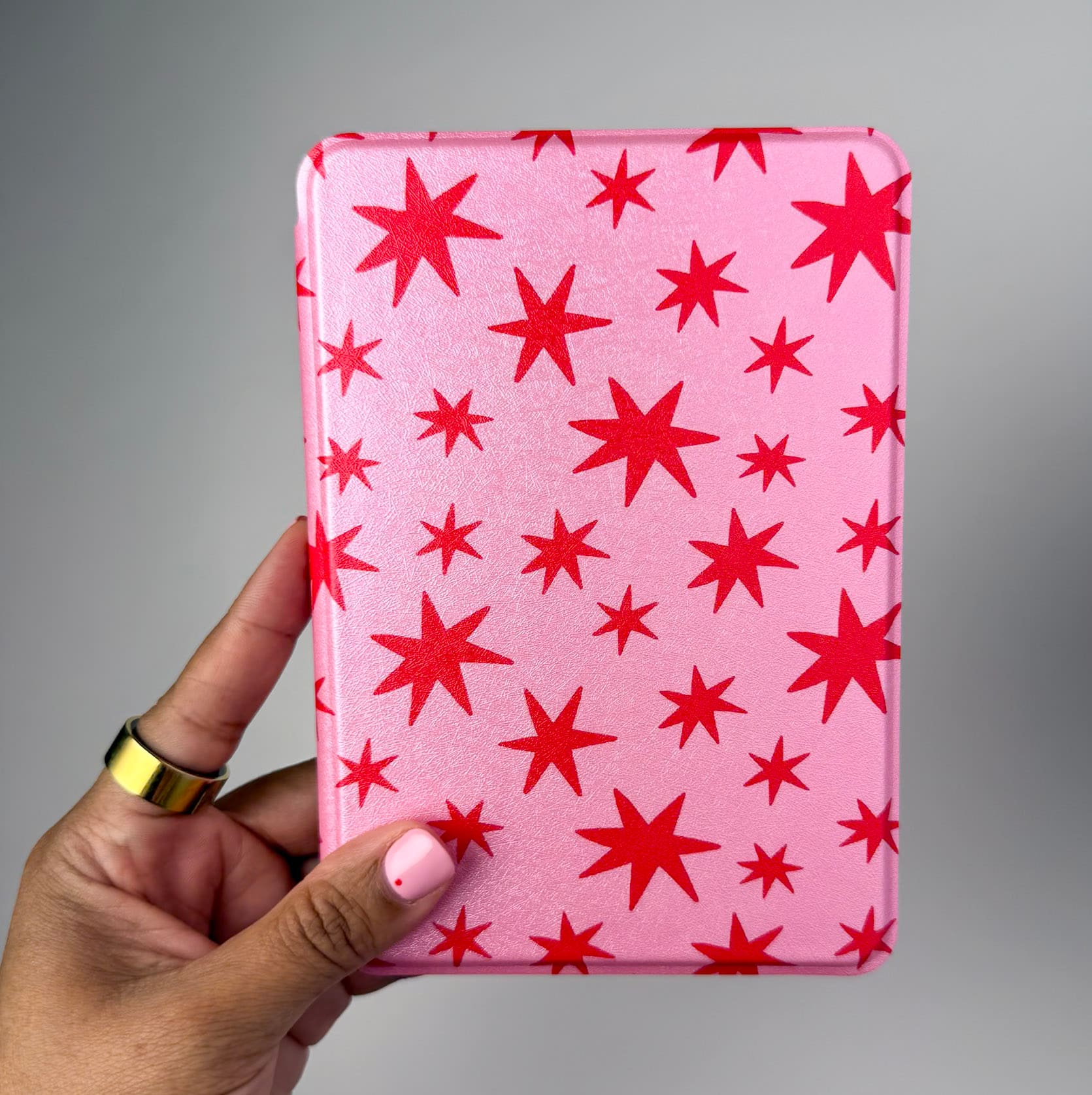 Pink case with red star pattern held by a hand against a gray background