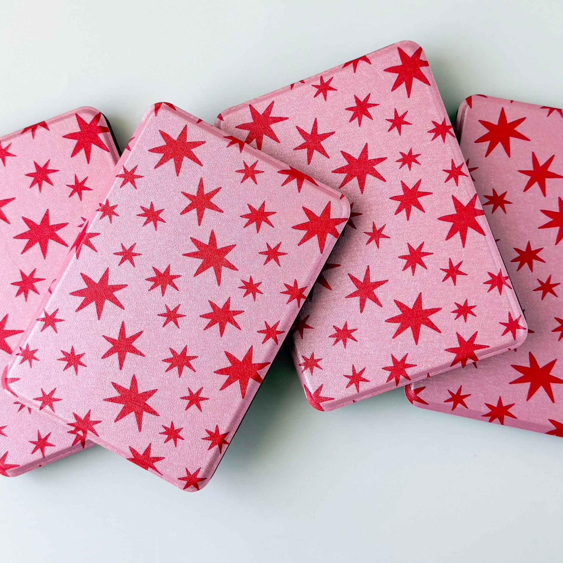 Kindle cases printed with red stars on a pink background. Kindle cases are spread out on a white background 
