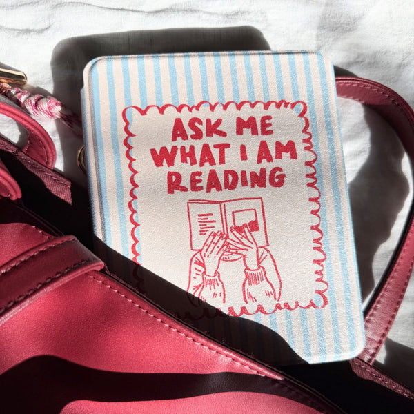 Kindle case with 'Ask Me What I Am Reading' text and illustration on a pink bag.