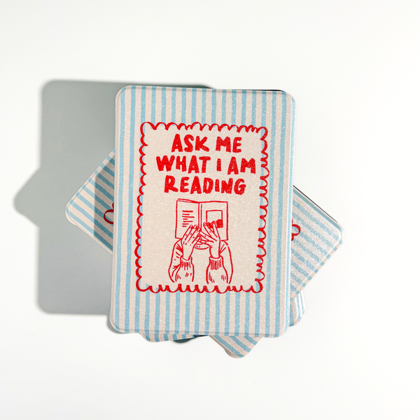 A stack of Kindle cases in a striped blue-and-white sleeve, with the top card showing red text that reads 'ASK ME WHAT I AM READING' above a red illustration of hands holding a book.