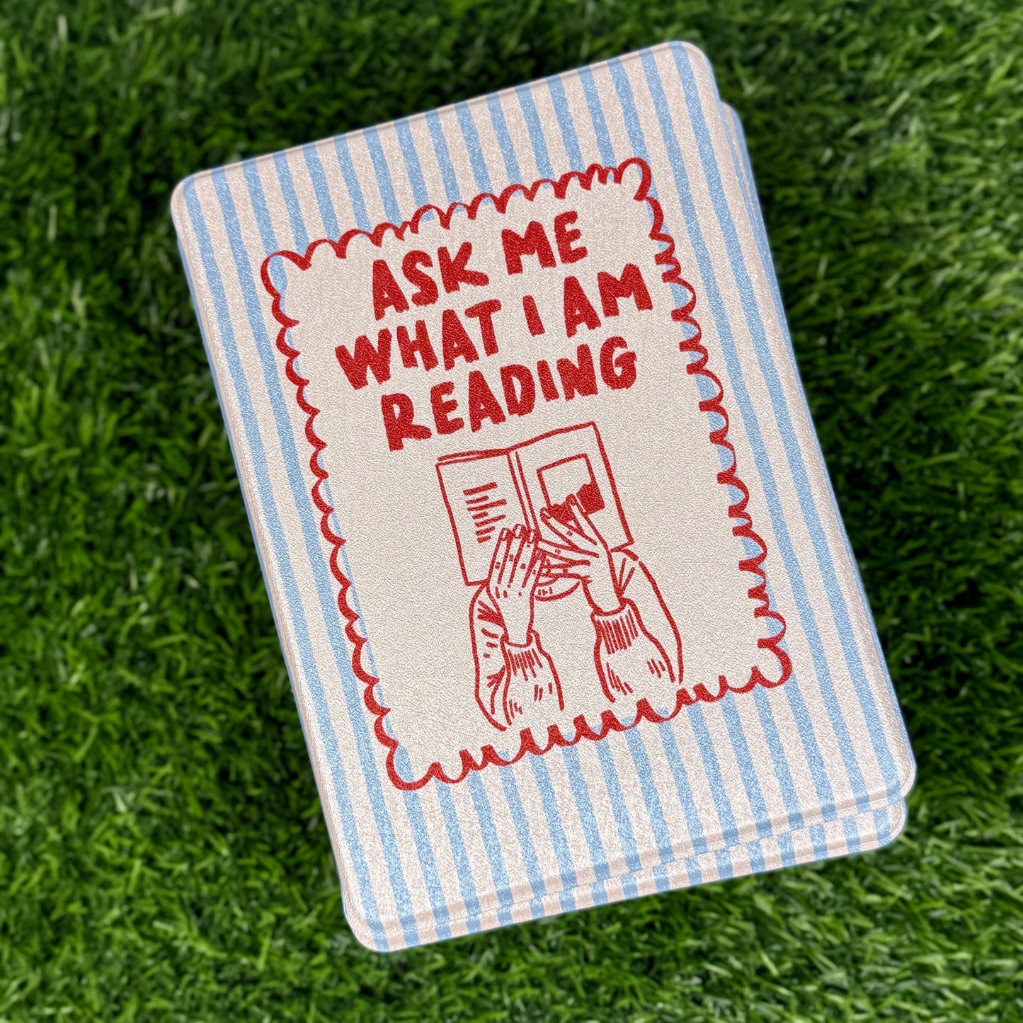 Notebook with 'Ask Me What I Am Reading' text on a grass background