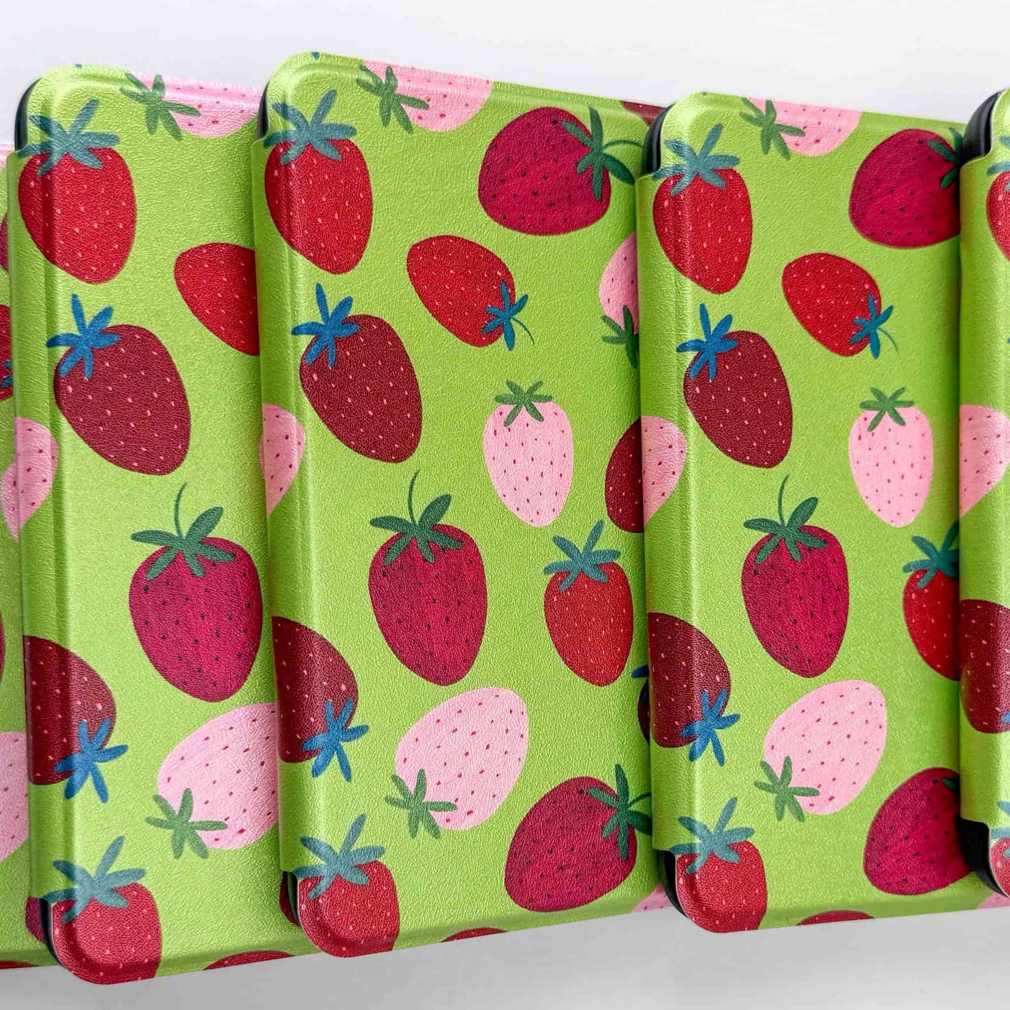 Set of four green kindle cases with strawberry pattern on a white background